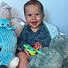 baby, smiling, child, toy, stuffed_animal, plush, blue_wall, happy, face, indoor, clothing, hand, sitting, baby_toy, cute, infant, playful, portrait, young_child, soft_toy