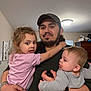 child, baby, man, family, indoor, holding, parent, father, casual, clothing, love, affection, portrait, home, smile, curly_hair, watch, tattoo, cap, window