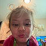 Amelia is registered to the contest to win money with this photo: child, face, close_up, curly_hair, funny_face, puckered_lips, pink_shirt, lanyard, indoor, living_room, television, animation, cartoon, furniture, home, portrait, expression, cute, messy_hair, playful