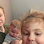 child, baby, adult, family, indoor, smile, curly_hair, blonde_hair, casual_clothing, person, portrait, hand, face, playing, holding, expression, closeup, candid, parent, home