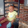 blue_bows, brick_wall, casual, child, cushion, cute, daylight, footwear, front_portrait, hair, happy, home, outdoor, person, rocking_chair, sitting, smile, sunny, toddler, yellow_clothing