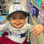 Makari joined the competition — help win amazing prizes! toddler, child, shopping_cart, hat, smile, baby_products, aisle, store, clothing, safety_belt, hand, face, person, retail, sitting, cute, cap, happy, indoor, playful