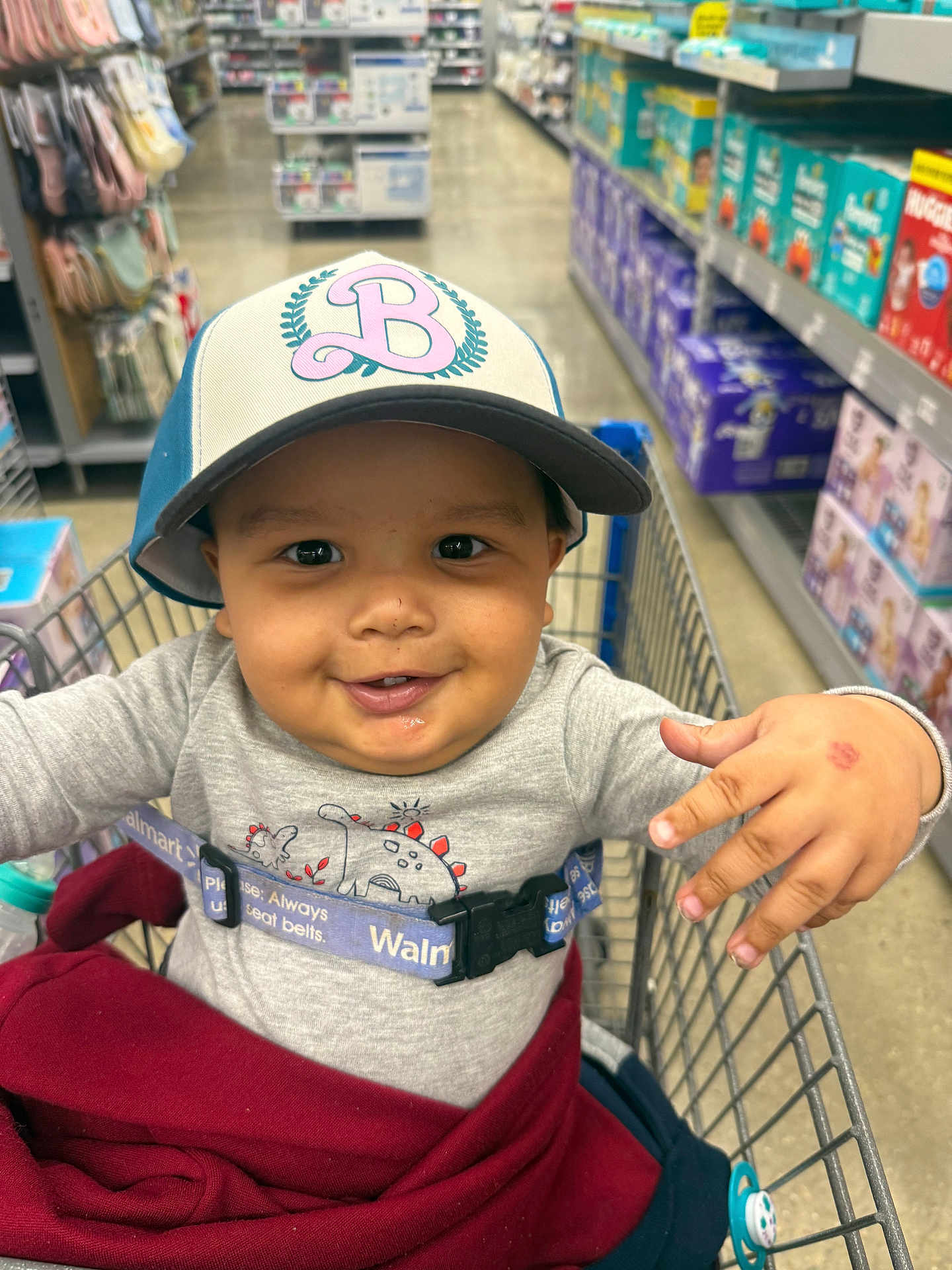 Makari joined the competition — help win amazing prizes! toddler, child, shopping_cart, hat, smile, baby_products, aisle, store, clothing, safety_belt, hand, face, person, retail, sitting, cute, cap, happy, indoor, playful