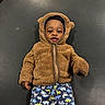 baby, child, hoodie, brown, fuzzy, dinosaur_pants, lying_down, cute, smiling, face, infant, clothing, texture, black_background, playful, curious, person, indoor, young_child, zipper