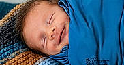 Declan joined the competition — help win amazing prizes! baby, newborn, smiling, sleeping, blue_blanket, knitted_blanket, cozy, portrait, face, infant, peaceful, resting, cute, child, wrapped, soft, closeup, young, indoors, warm