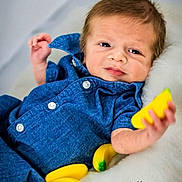 Declan joined the competition — help win amazing prizes! baby, blue_clothing, toy_banana, yellow, fluffy_surface, infant, cute, portrait, child, playful, relaxed, indoor, soft_texture, smile, face, hand, small_bananas, cozy, curious, closeup