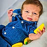 baby, blue_clothing, toy_banana, yellow, fluffy_surface, infant, cute, portrait, child, playful, relaxed, indoor, soft_texture, smile, face, hand, small_bananas, cozy, curious, closeup