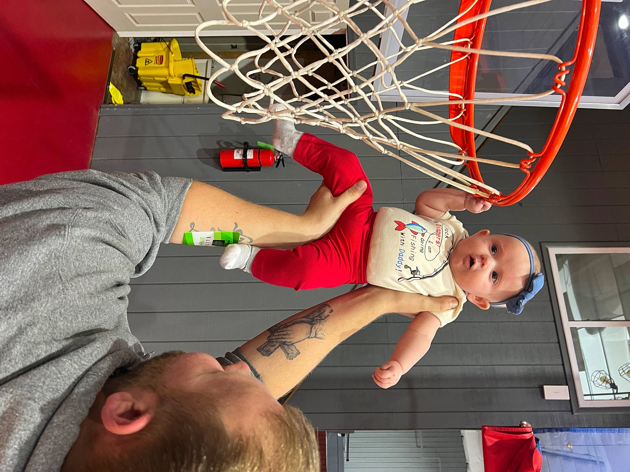 Zoe is registered to the contest to win money with this photo: arm, ball, basketball_hoop, child, elbow, fun, human_leg, leisure, muscle, net, person, play, player, room, shorts, sports_equipment, t_shirt, thigh, toddler, visual_arts