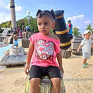 Christiana joined the competition — help win amazing prizes! child, toddler, outdoor, playground, water_park, barrel, pink_shirt, shorts, people, sunny, daytime, trees, blue_sky, play, hat, footwear, expression, park, fun, summer