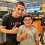 apparel_store, casual_clothing, child, clothing_rack, friendship, glasses, happy, indoor, male, person, portrait, retail, shopping, short_hair, smile, sportswear, store, teenager, thumbs_up, tshirt