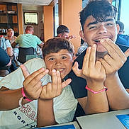 Clément participe au concours pour gagner de l'argent avec cette photo : background, boy, bracelet, casual, child, face, friendship, fun, glass, hair, hand_gesture, happy, indoor, lunch, menu, people, restaurant, seated, smile, table