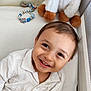 baby, bed, child, closeup, comfort, cozy, cute, face, happy, indoors, pacifier_clip, person, playful, plush_toy, portrait, smiling, soft_surface, toddler, white_shirt, young_child