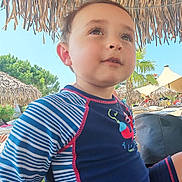 Malo a rejoint le concours — aidez-le/la à gagner de superbes lots ! child, boy, swimwear, blue, striped, outdoor, sunny, umbrella, thatched_roof, tropical, palm_tree, beach, poolside, curious, young, casual, daylight, vacation, relaxation, portrait