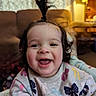 toddler, child, smiling, happy, indoor, portrait, baby, hair_tie, sweater, patterned_clothing, lamp, couch, living_room, cute, face, person, young_child, playful, joyful, fun