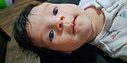 Scarlett is registered to the contest to win money with this photo: baby, closeup, face, infant, child, lying_down, eyes, hair, white_clothing, patterned_clothing, indoors, floor, wooden_floor, curious, portrait, person, young_child, expression, soft_lighting, casual
