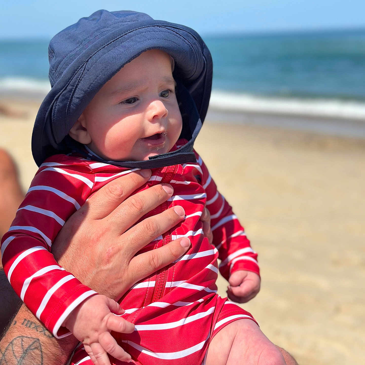 Joseph is registered to the contest to win money with this photo: baby, beach, bodypart, cap, clothing, coast, face, finger, hand, hat, head, nature, outdoors, person, photography, portrait, sea, shoreline, skin, water
