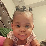 Marlie joined the competition — help win amazing prizes! baby, infant, toddler, cute, smile, face, eyes, cheeks, hair_buns, onesie, closeup, portrait, bedroom, headboard, pillow, indoors, lying_down, happy, skin, child