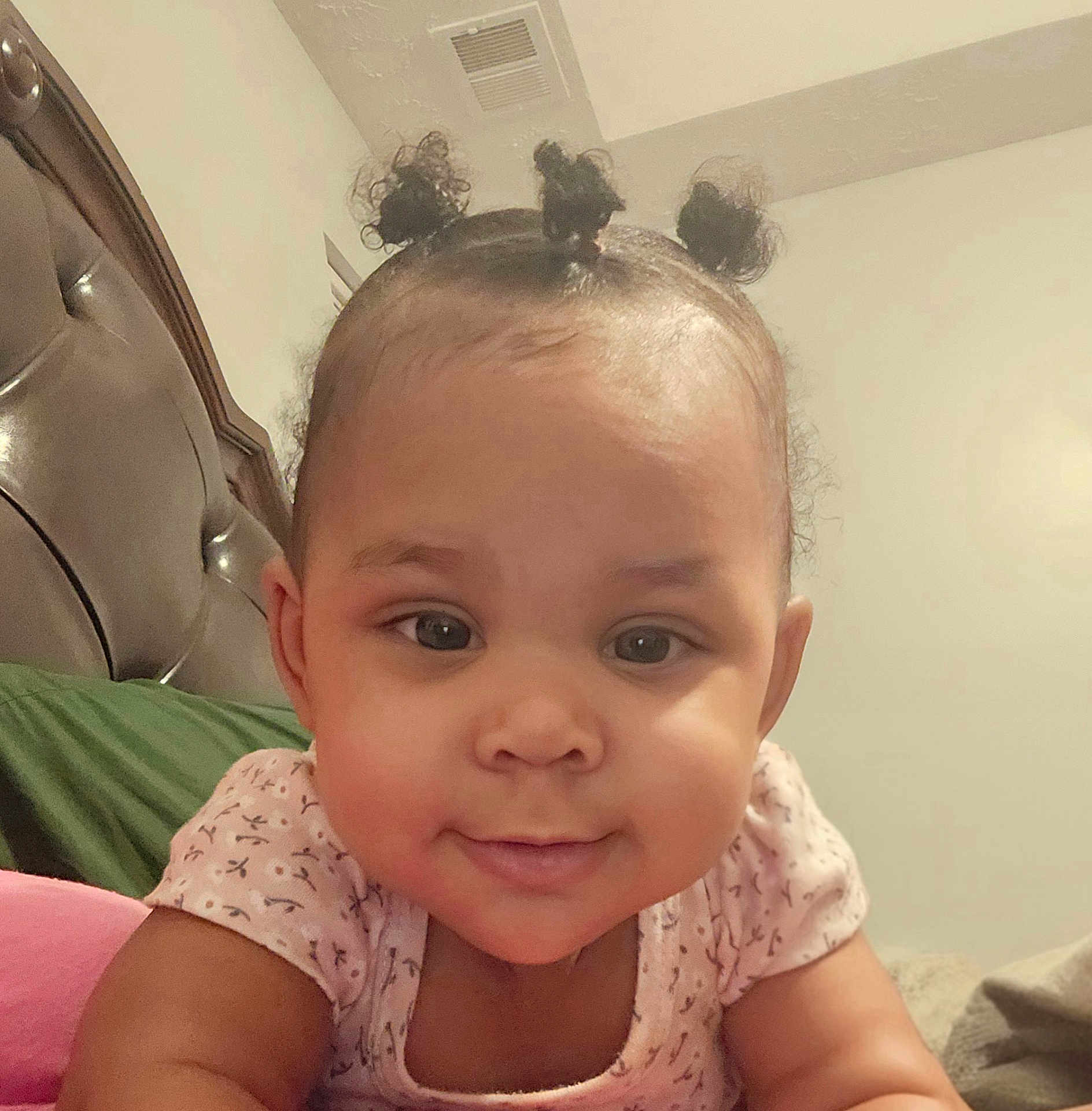 Marlie joined the competition — help win amazing prizes! baby, infant, toddler, cute, smile, face, eyes, cheeks, hair_buns, onesie, closeup, portrait, bedroom, headboard, pillow, indoors, lying_down, happy, skin, child