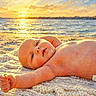 baby, infant, child, portrait, beach, ocean, sunset, sunlight, blanket, diaper, lying_down, outdoor, seaside, water, sky, horizon, warm_colors, smiling, reaching, painterly