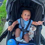 Carlos joined the competition — help win amazing prizes! baby, stroller, blue_onesie, socks, plush_toy, baby_bottle, outdoor, sidewalk, grass, happy, smiling, child, infant, seatbelt, black_stroller, person, cute, portrait, baby_clothing, playful