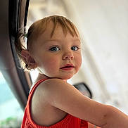 Maelynn is registered to the contest to win money with this photo: toddler, child, blue_eyes, orange_clothing, portrait, indoor, curious, face, hair, skin, person, young_child, cute, expression, natural_light, blurry_background, small_pony_tail, sleeveless, looking_back, close_up