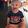 Maelynn is registered to the contest to win money with this photo: toddler, child, smiling, happy, sitting, black_tshirt, text_on_clothing, indoor, blurred_background, shorts, cute, person, face, blue_eyes, light, hair, hand, legs, casual, young_child