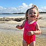 Maelynn is registered to the contest to win money with this photo: toddler, child, swimsuit, pink, water, beach, smiling, happy, sunny, sky, clouds, bracelet, hair, standing, shallow_water, outdoor, portrait, cute, summer, playful