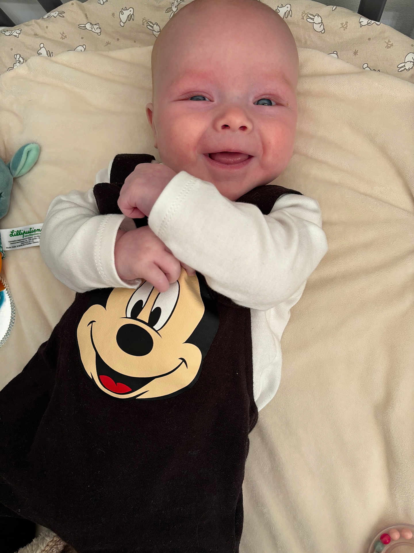 Roméo participe au concours pour gagner de l'argent avec cette photo : baby, infant, smiling, mickey_mouse, blanket, onesie, plush_toy, crib, cheeks, eyes, hand, portrait, closeup, happy, newborn, lying_down, nursery, soft_fabric, clothing, bunny_prints