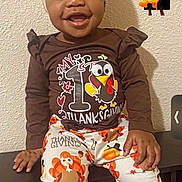 Kamira is registered to the contest to win money with this photo: toddler, child, smiling, thanksgiving, holiday_clothing, headwrap, bench, indoor, happy, cute, portrait, person, wall, cartoon_sticker, pumpkin, turkey, long_sleeve_shirt, pants, colorful, festive