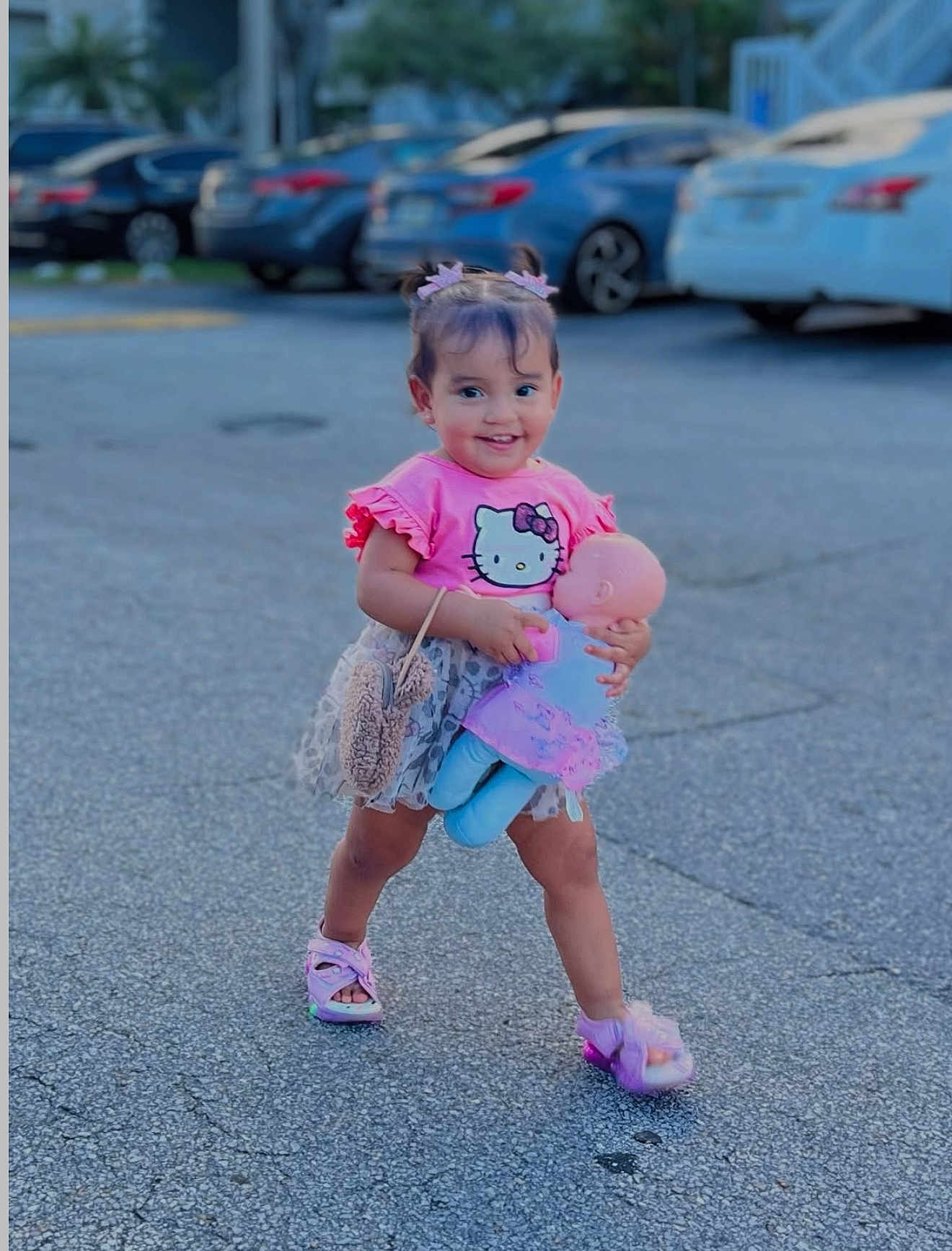 Zara Cataleya joined the competition — help win amazing prizes! toddler, child, girl, toy, doll, pink, sandals, hair_clips, smiling, parking_lot, sidewalk, purse, shorts, outdoor, cute, happy, walking, clothing, person, daytime