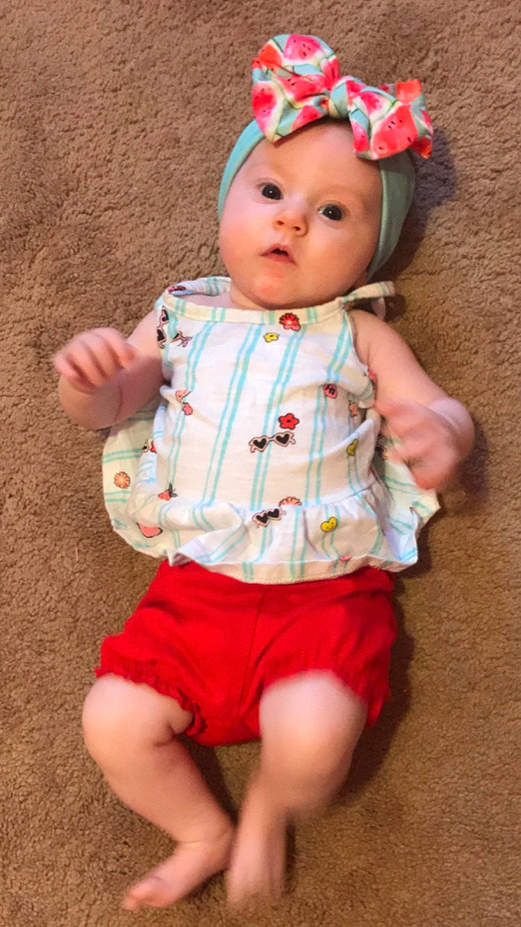 Stormi is registered to the contest to win money with this photo: baby, baby_products, baby_toddler_clothing, cheek, child, hair_accessory, headband, headgear, headwear, person, pink, play, product, sleeve, surprise, toddler