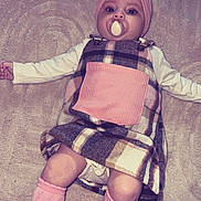 Jasmine is registered to the contest to win money with this photo: baby, pacifier, pink_bow, plaid_dress, pink_pocket, pink_socks, blanket, lying_down, infant, cute, headwear, child, soft_texture, indoors, portrait, adorable, young_child, fashion, cozy, warm_clothing