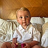 Hardin joined the competition — help win amazing prizes! toddler, child, bed, pillow, wooden_headboard, white_polo_shirt, beige_shorts, pink_objects, rosy_cheeks, blue_eyes, indoor, seated, cute, portrait, person, casual_clothing, soft_lighting, home, young_child, holding