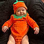 Lilith is registered to the contest to win money with this photo: baby, infant, costume, orange, hat, green, leaf, cute, smile, face, child, black_cushion, plush, comfortable, indoors, sitting, legs, arms, skin, portrait