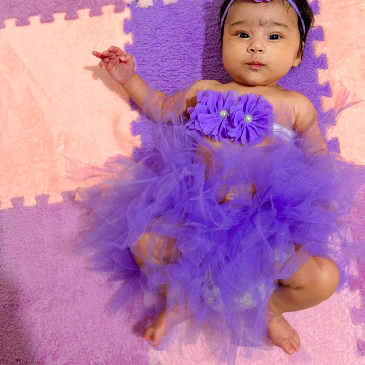 Urvika joined the competition — help win amazing prizes! baby, child, colorful_background, cute, decorative_clothing, flower_accessory, footwearless, happy, headband, indoor, infant, lying_down, person, play_mat, portrait, purple_tutu, puzzle_mat, smiling, soft_texture, young_child