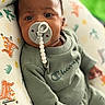 baby, infant, pacifier, clothing, green_outfit, cushion, patterned_fabric, cute, portrait, indoors, child, person, closeup, cozy, soft_lighting, small_hands, head, curious, sitting, casual_wear