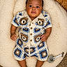 baby, infant, crochet_outfit, bear_pattern, cushion, pacifier, indoor, curious, child, cute, patterned_clothing, footwear_free, lying_down, soft_texture, plush, portrait, skin, hand, head, eyes