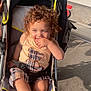 Kaïs participe au concours pour gagner de l'argent avec cette photo : child, toddler, stroller, curly_hair, outdoor, sunlight, clothing, shoes, socks, cute, baby, sitting, hand, face, pavement, casual, summer, young_child, daylight, portrait