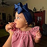 Kahlani is registered to the contest to win money with this photo: baby, child, indoor, headband, bow, striped_dress, hand, person, curious, portrait, skin, face, cute, infant, young_child, holding, room, furniture, red, blue