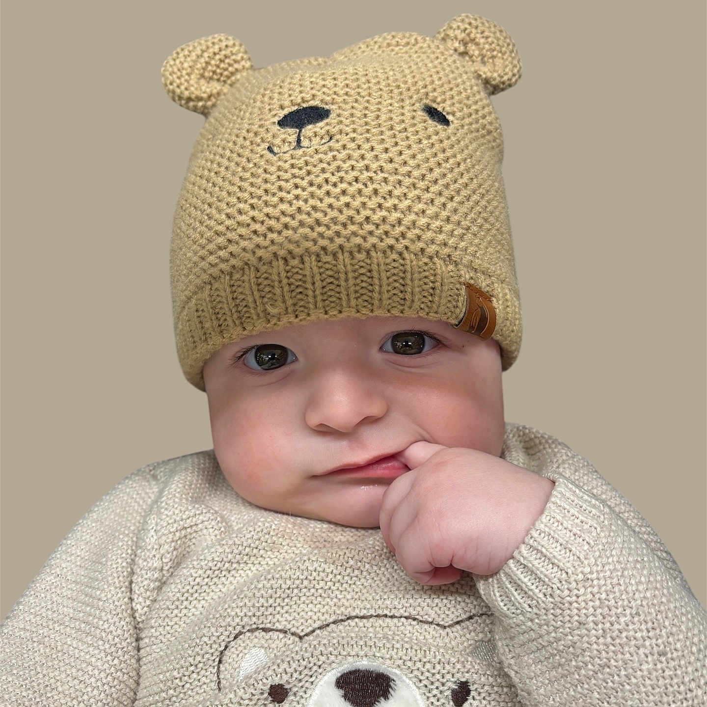 Rome Alexander is registered to the contest to win money with this photo: adorable, baby, bear_hat, beige_clothing, child, child_fashion, close_up, cute, expression, face, finger_in_mouth, hand, infant, knitted_hat, neutral_background, portrait, soft_lighting, sweater, warm_clothing, young_child