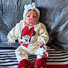 apparel, baby, blanket, child, clothing, cute, face, headband, indoors, infant, mickey_mouse, minnie_mouse, pacifier, person, pillow, red_slippers, resting, sitting, soft, striped