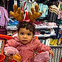 Lyana participe au concours pour gagner de l'argent avec cette photo : antler_headband, bread, child, clothing_store, curious, curly_hair, cute, fashion, holding_food, indoor, orange_cart, pink_jacket, portrait, retail, shopping, shopping_cart, store_shelves, toddler, winter_clothing, young_child