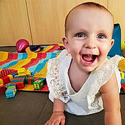 Lison participe au concours pour gagner de l'argent avec cette photo : baby, child, smiling, crawling, white_dress, lace, indoor, play_mat, colorful_blocks, toys, happy, blue_eyes, face, person, cute, floor, wooden_cabinet, playtime, childhood, bright