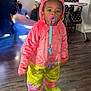 Miracle is registered to the contest to win money with this photo: toddler, child, costume, pacifier, indoor, floor, wooden_floor, fish_tank, portrait_painting, high_chair, baby_gear, colorful_clothing, plush, person, curious, standing, room, bright_clothing, yellow_shoes, pink_outfit