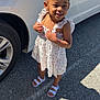 Miracle is registered to the contest to win money with this photo: accessories, asphalt, car, child, cute, dress, earrings, fashion, hair_buns, happy, outdoor, parking_lot, person, smiling, standing, sunlight, toddler, vehicle, white_sandals, young_child