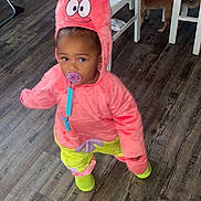Miracle joined the competition — help win amazing prizes! toddler, child, costume, pacifier, indoor, wood_floor, dog, table, chair, white_furniture, pink_clothing, yellow_clothing, hood, funny_face, baby, person, flooring, puppy, home, curious_pet