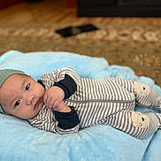 Liam is registered to the contest to win money with this photo: baby, blanket, carpet, child, comfortable, cute, expression, face, floor, hands, hat, indoors, infant, knitted_hat, lying_down, patterned_carpet, portrait, soft_texture, striped_onesie, warm_lighting