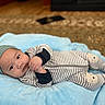 baby, infant, blanket, striped_onesie, hat, knitted_hat, face, hands, floor, carpet, patterned_carpet, soft_texture, lying_down, cute, indoors, warm_lighting, expression, portrait, child, comfortable