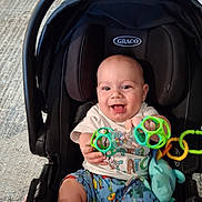Bradley joined the competition — help win amazing prizes! baby, car_seat, toy, smiling, indoor, child, graco, clothing, shorts, white_shirt, happy, infant, seat, playful, colorful, hand, face, person, cute, young