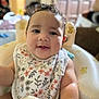 arm, baby, baby_seat, bib, child, closeup, curly_hair, cuteness, face, floral_pattern, furniture, happy, home, indoor, infant, person, portrait, sippy_cup, smiling, teddy_bear_print